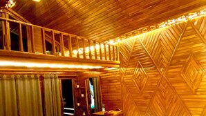 A hotel room with a wooden ceiling, a bed with white bedding, a small table, and a chair. - Meghsomudro Eco Resort Sajek (Sajek)
