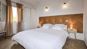 Un dormitorio con una cama grande, dos mesitas de noche con lámparas, un cabecero de madera y una ventana con cortinas.