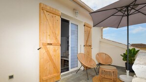 Un patio con contraventanas de madera, sillas de mimbre, una mesa redonda y una planta en maceta.