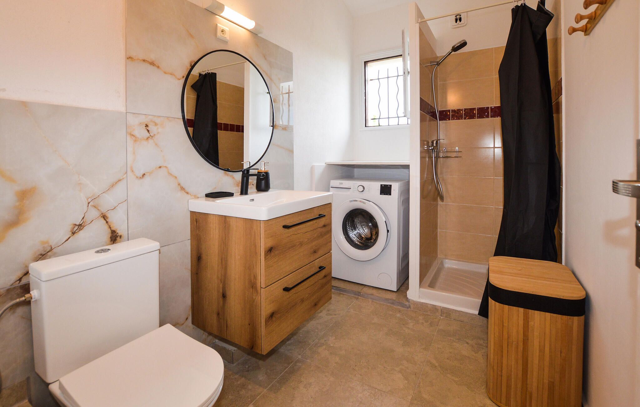 Une salle de bain comprenant des toilettes, un lavabo, un miroir, un lave-linge, une douche et un meuble en bois.