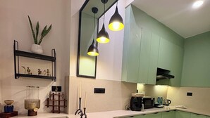 A modern kitchen with green cabinets, a white countertop, two black bar stools, and pendant lighting. - Indigo - Luxury Bathtub Studio at Golf Course Rd (Gurugram)