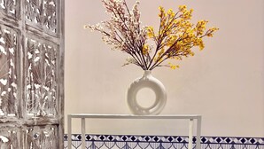 A bookshelf with decorative items and a vase of flowers. - Indigo - Luxury Bathtub Studio at Golf Course Rd (Gurugram)
