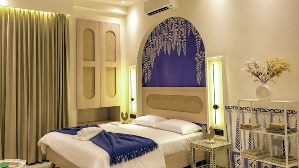 A modern hotel room with a large bed, a ceiling fan, a decorative wall, and a small side table. - Indigo - Luxury Bathtub Studio at Golf Course Rd (Gurugram)