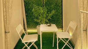 A corner room with a green artificial grass floor, a white table with two chairs, a potted plant, and a wall with a green artificial hedge. - Indigo - Luxury Bathtub Studio at Golf Course Rd (Gurugram)