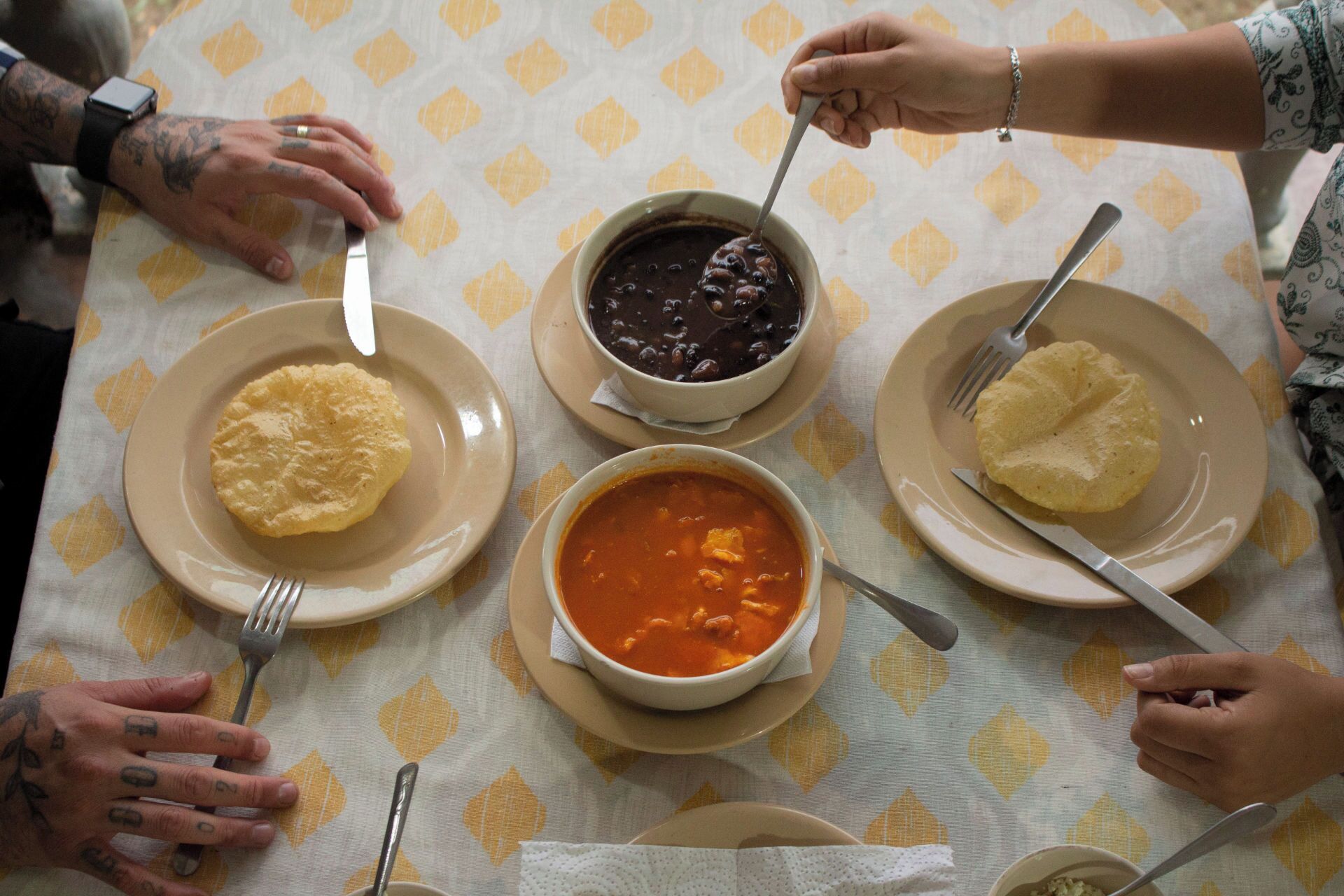 A group of people dining around a table with plates of food, forks, and a watch on someone's wrist.