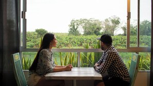 Two people seated at a table with a view of a green landscape through large windows.