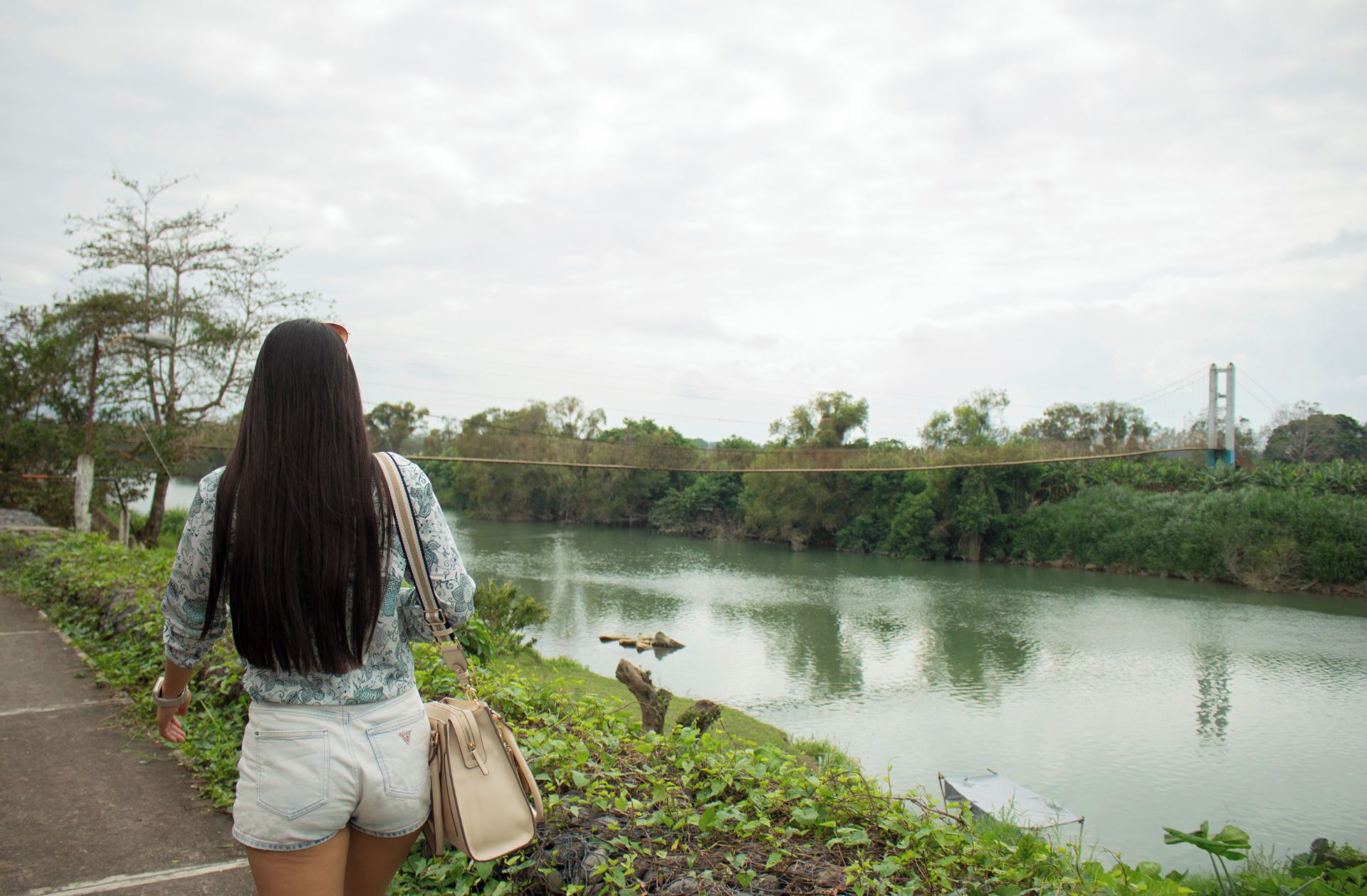 A person standing by a river with a bridge in the background.