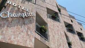 A hotel named 'Hotel Champlitte' with a modern facade, multiple balconies with plants, and a clear sky.