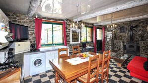 A rustic kitchen with stone walls, a wooden dining table, and a built-in washing machine. - Authentique maison Montagne (Nohèdes)