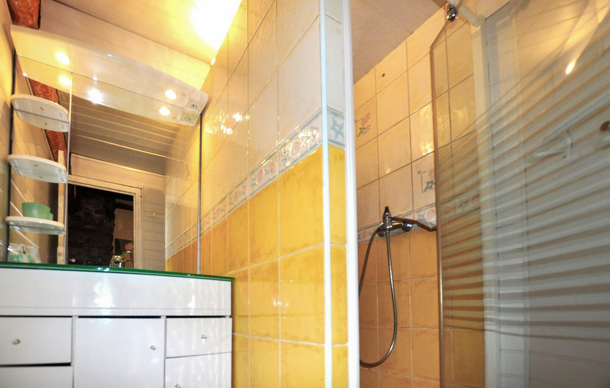 Un bany amb dutxa, mirall i un lavabo amb taulell de vidre.