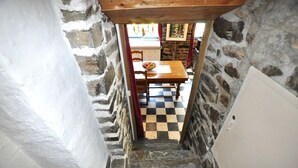 A narrow stairway with stone walls, leading to a room with a checkered floor and a wooden table. - Authentique maison Montagne (Nohèdes)