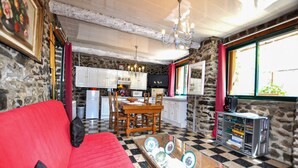 A cozy interior with a red sofa, checkered floor, stone walls, a kitchen with white cabinets, and a bookshelf. - Authentique maison Montagne (Nohèdes)