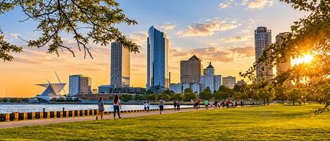Un paisaje urbano con edificios modernos, un río y un parque donde pasean personas.