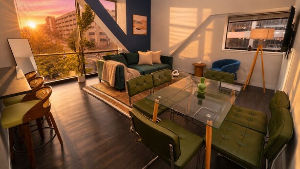 A modern living room with a glass dining table, green sofas, and a city view.