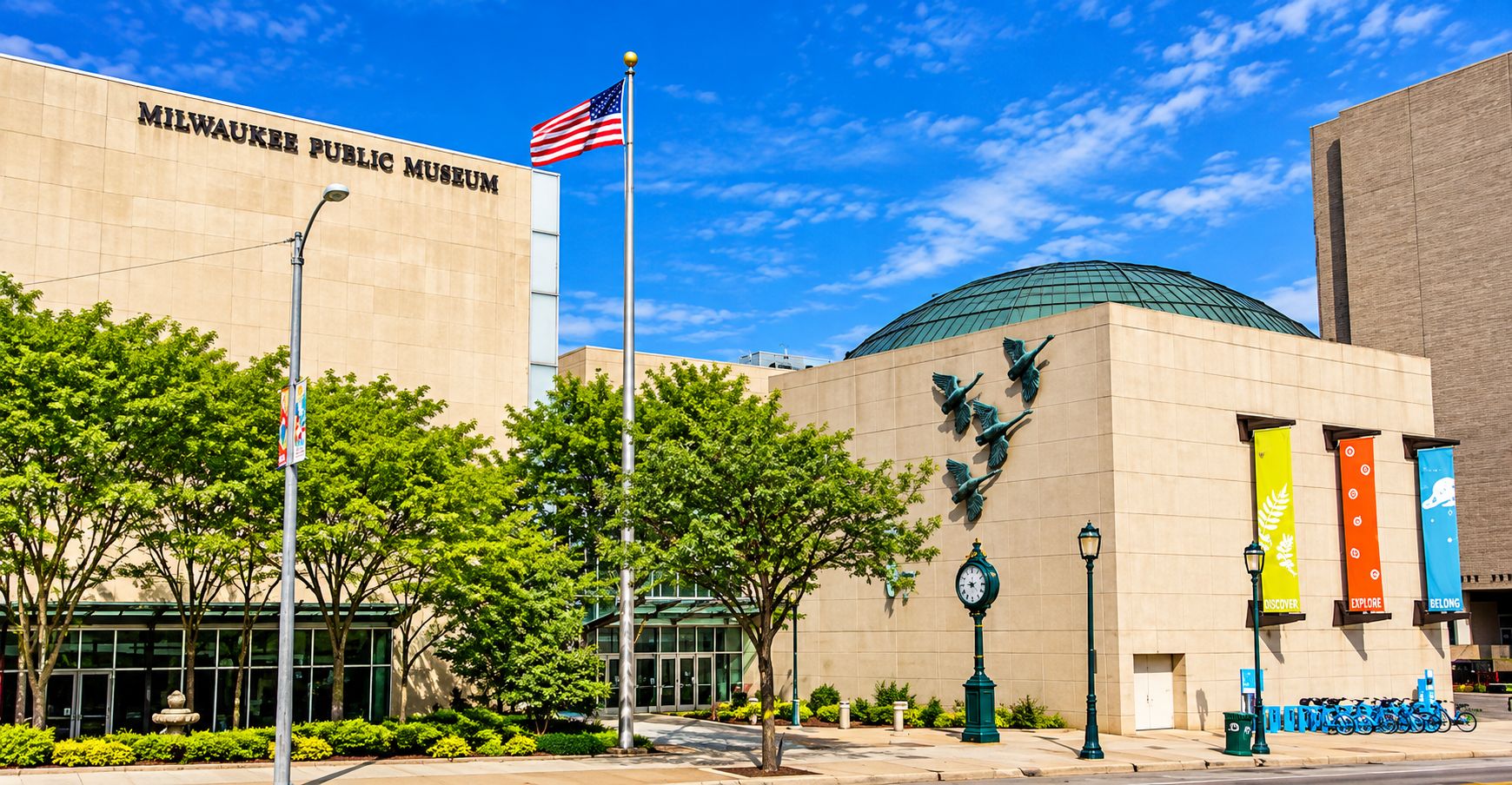 Il Museo Pubblico di Milwaukee con una grande bandiera americana, una scultura di un uccello e degli striscioni.