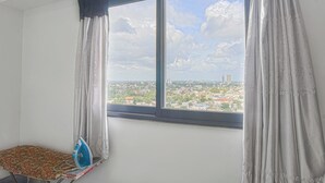 Ein Zimmer mit großem Fenster, Bügelbrett und Blick auf eine Stadtlandschaft.