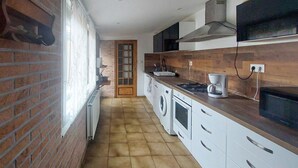 A kitchen with a brick wall, a wooden countertop, a washing machine, a stove, and a coffee maker. - Jolie maison avec cour (Grand-Fort-Philippe)