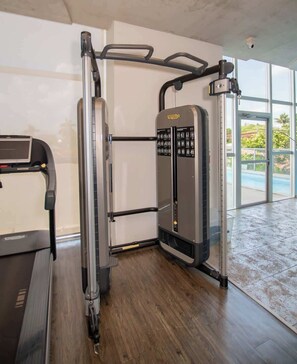 A gym with a treadmill, weight machines, and a large window offering a view of the outdoors. - Corporate Stays Miami (Asunción)