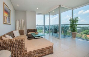Ein modernes Wohnzimmer mit einer Couch, einem Glastisch und Blick auf eine Stadtlandschaft durch große Fenster.