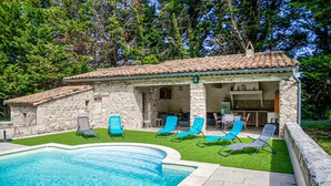Un edificio de piedra con techo de tejas, piscina y mobiliario de exterior.