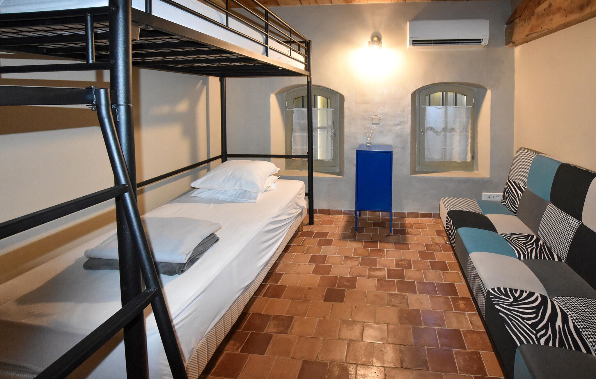 A bunk bed room with a blue cabinet, two arched windows, and a patterned sofa.
