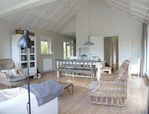 A spacious room with a dining table, chairs, a bookshelf, and a wicker sofa. - Bungalow Near Dishoek Beach (Koudekerke)