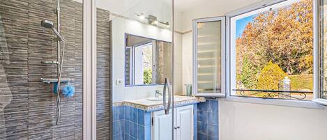 A modern bathroom with a glass shower enclosure, a large mirror, and a view of autumn foliage through a window.