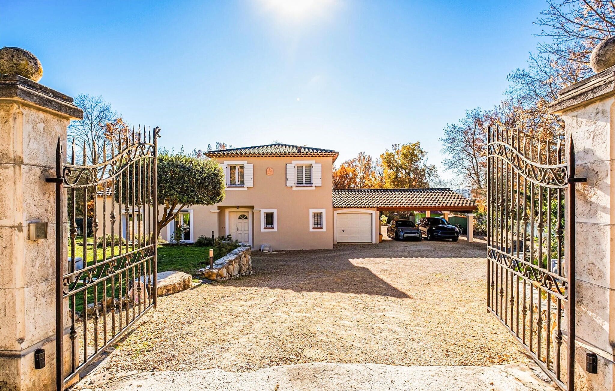 Une maison à deux étages avec une allée menant à une entrée fermée par un portail.
