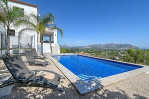 Ein Pool mit Liegestühlen, ein weißes Gebäude und Blick auf Berge.
