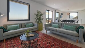 Ein modernes Wohnzimmer mit zwei grauen Sofas, einem roten Teppich mit Muster und einem großen Fenster.