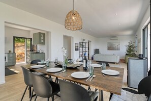A modern dining area with a wooden table set for four, a hanging woven light fixture, and a kitchen in the background. - Casa Zoe 4 pax - Pedreguer, Costa Blanca (Pedreguer)