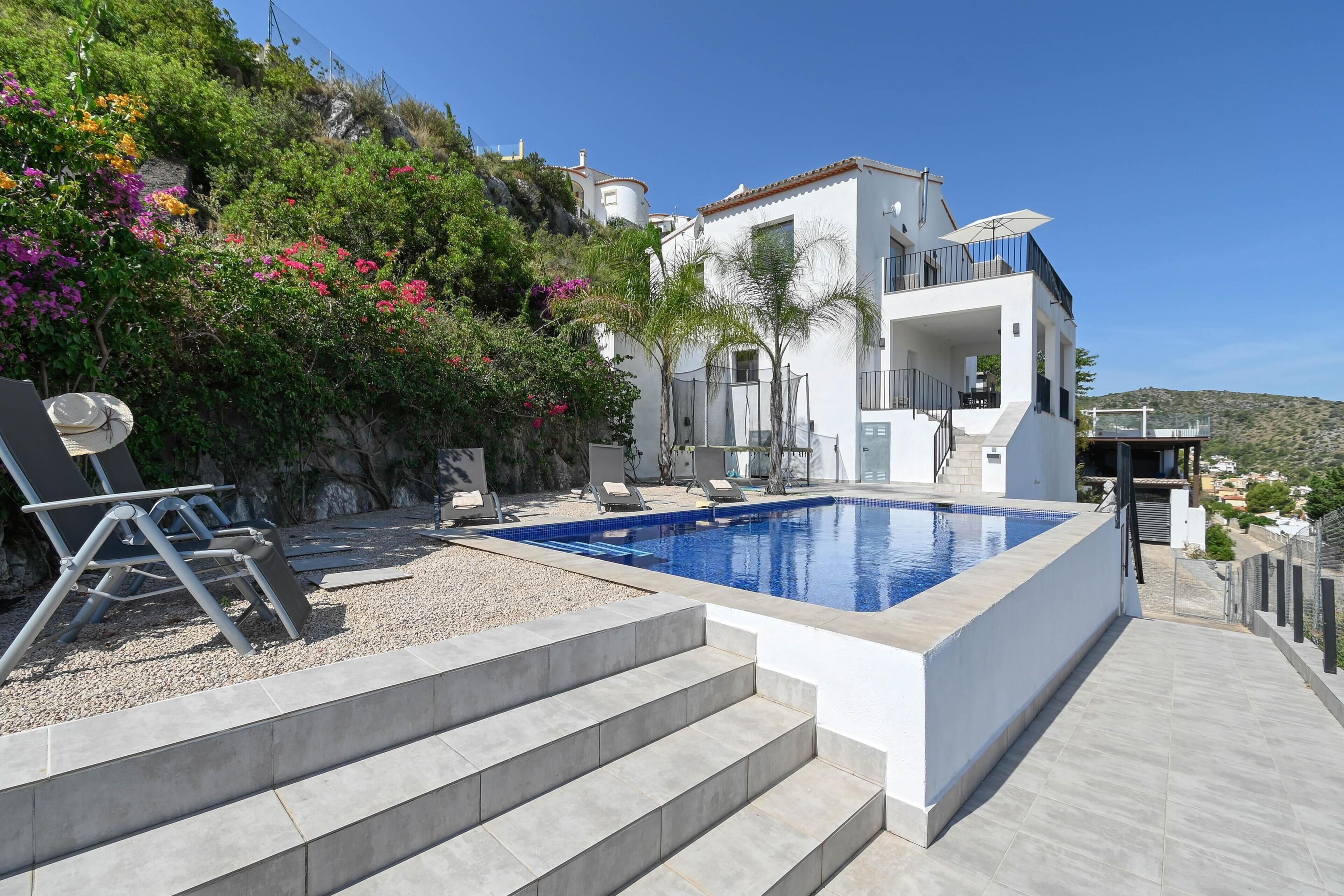 En modern villa med en swimmingpool, utomhusmöbler och utsikt över det omgivande landskapet.