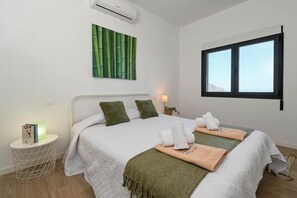A bedroom with a bed, pillows, a bedside table with a lamp, a wall-mounted air conditioner, and a window with a view. - Casa Zoe 4 pax - Pedreguer, Costa Blanca (Pedreguer)