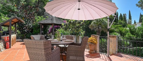 An outdoor patio with wicker furniture, a table, and a large umbrella.
