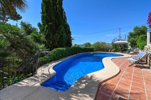 Ein Pool mit gewölbter Kante, umgeben von einer gefliesten Terrasse und Grünflächen.