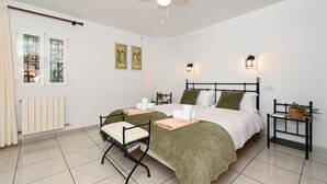 Quarto com duas camas, ventoinha no teto, luminárias na parede, radiador e janela com cortinas.
