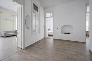 A spacious room with a wooden floor, a fireplace, and a sofa in the background.