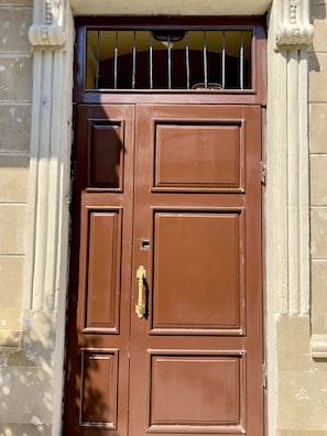 Une porte double en bois brun, surmontée d’une barre métallique, est intégrée à un bâtiment aux murs de pierre.