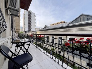 A balcony with a table and chairs, a decorative railing, and a view of buildings and flowers.
