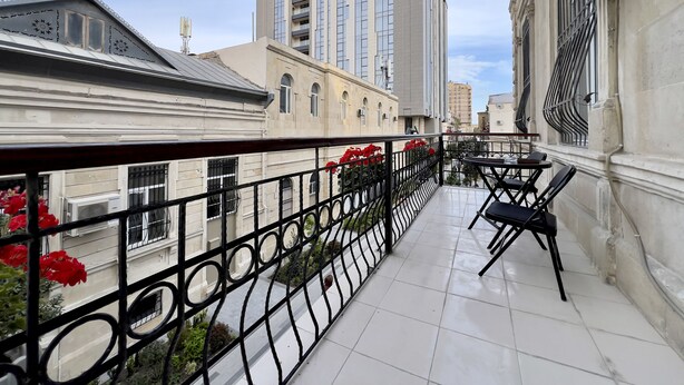 A balcony with a metal railing, a table with chairs, and a view of surrounding buildings.