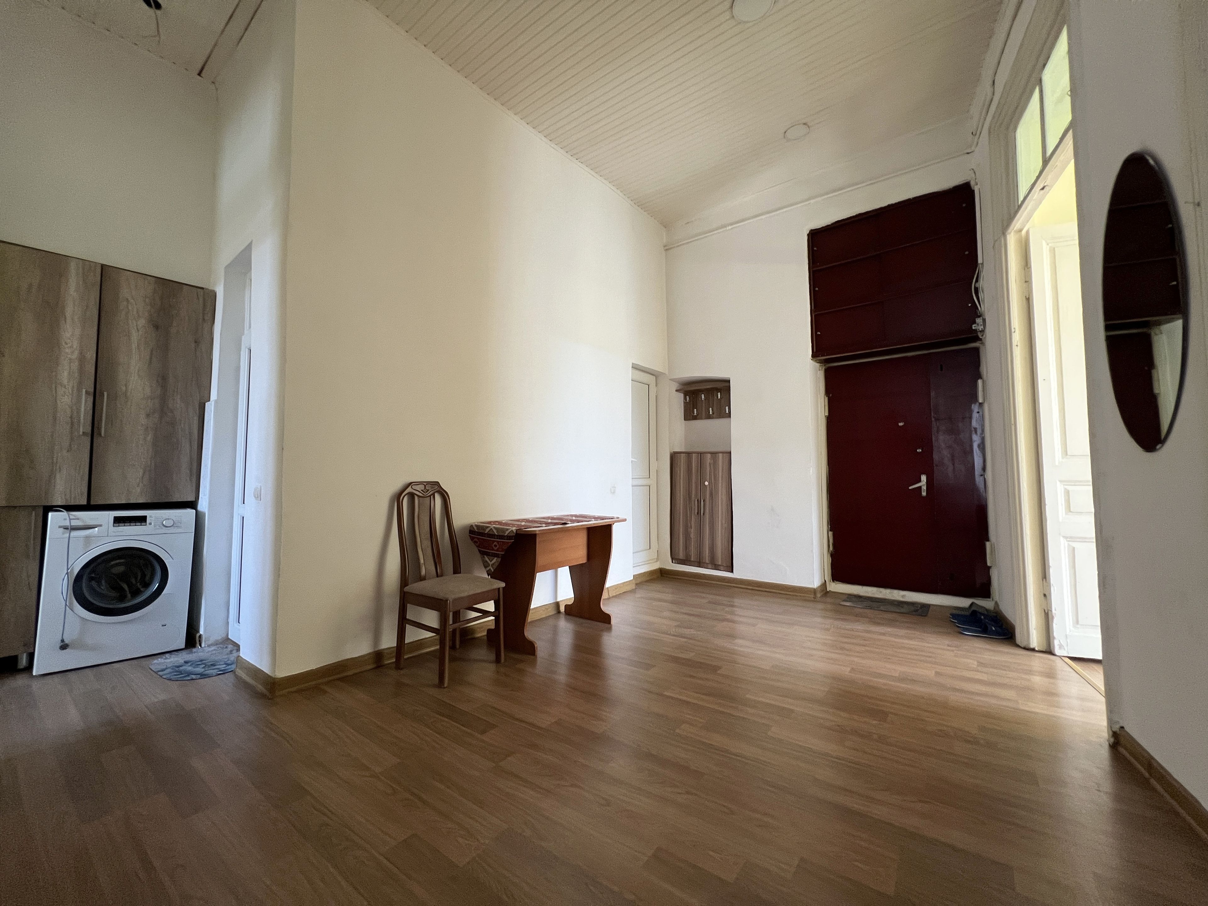 A spacious room with a wooden floor, a washing machine, a chair, a small table, and a wardrobe.