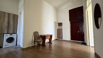 A spacious room with a wooden floor, a washing machine, a chair, a small table, and a wardrobe.