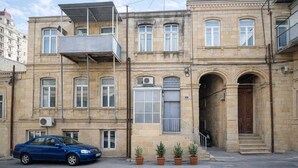 A multi-story building with a car parked in front, potted plants, and a staircase leading to an entrance.