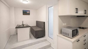 A compact kitchenette with a microwave, a small dining table, and a grey cushioned seating area.