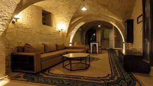 A cozy living room with a sofa, coffee table, and patterned rug, under a vaulted stone ceiling with arched alcoves.