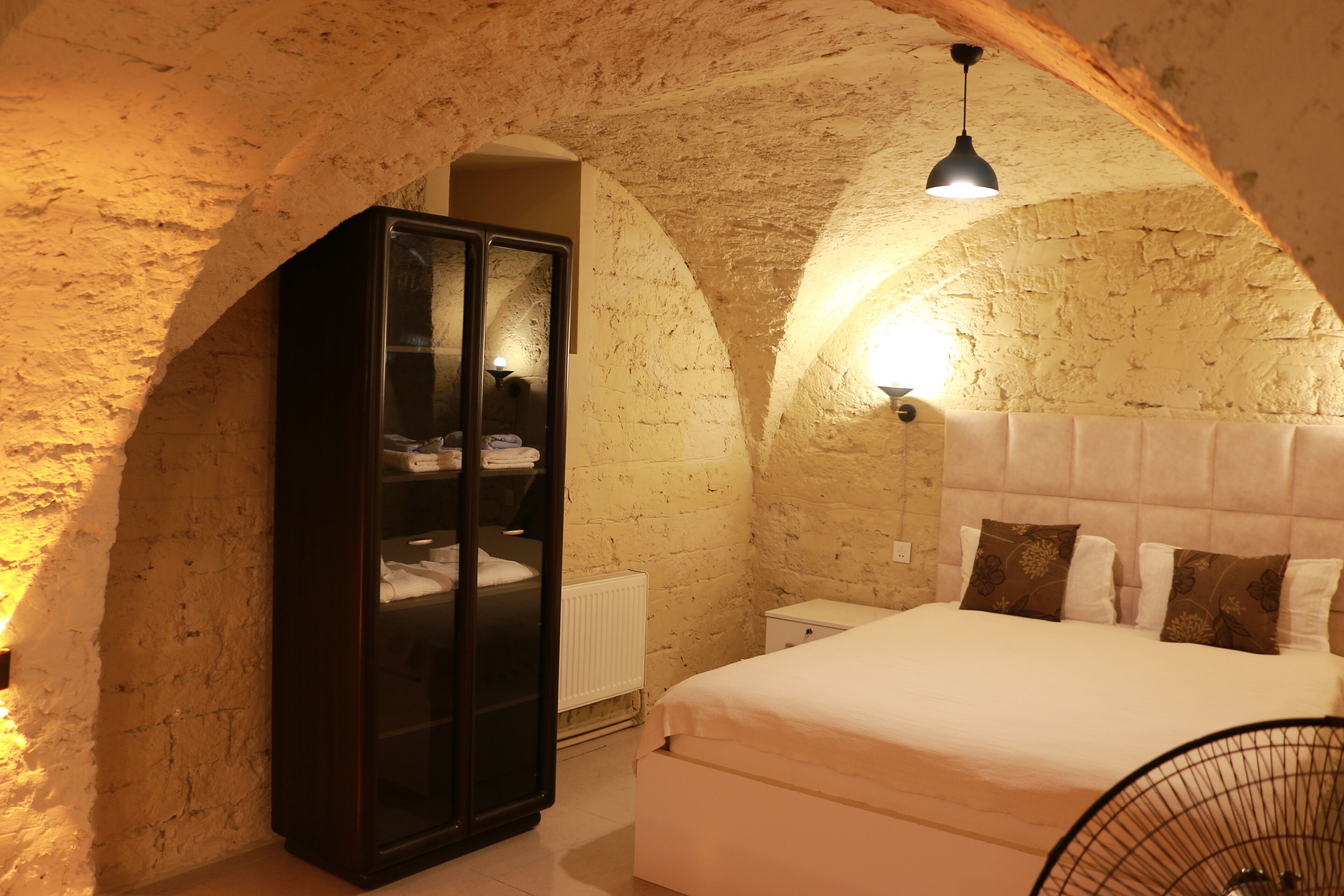 Une chambre avec un mur en pierre, un lit avec une tête de lit, une armoire et un luminaire suspendu.