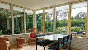 Une pièce lumineuse, avec une table à manger, des chaises et de grandes fenêtres donnant sur un jardin.