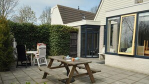 Une terrasse avec une table et des chaises en bois, une statue et une haie.