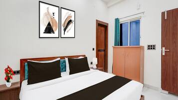 A hotel room with a bed, a nightstand with a lamp, a wardrobe, and two framed artworks on the wall.