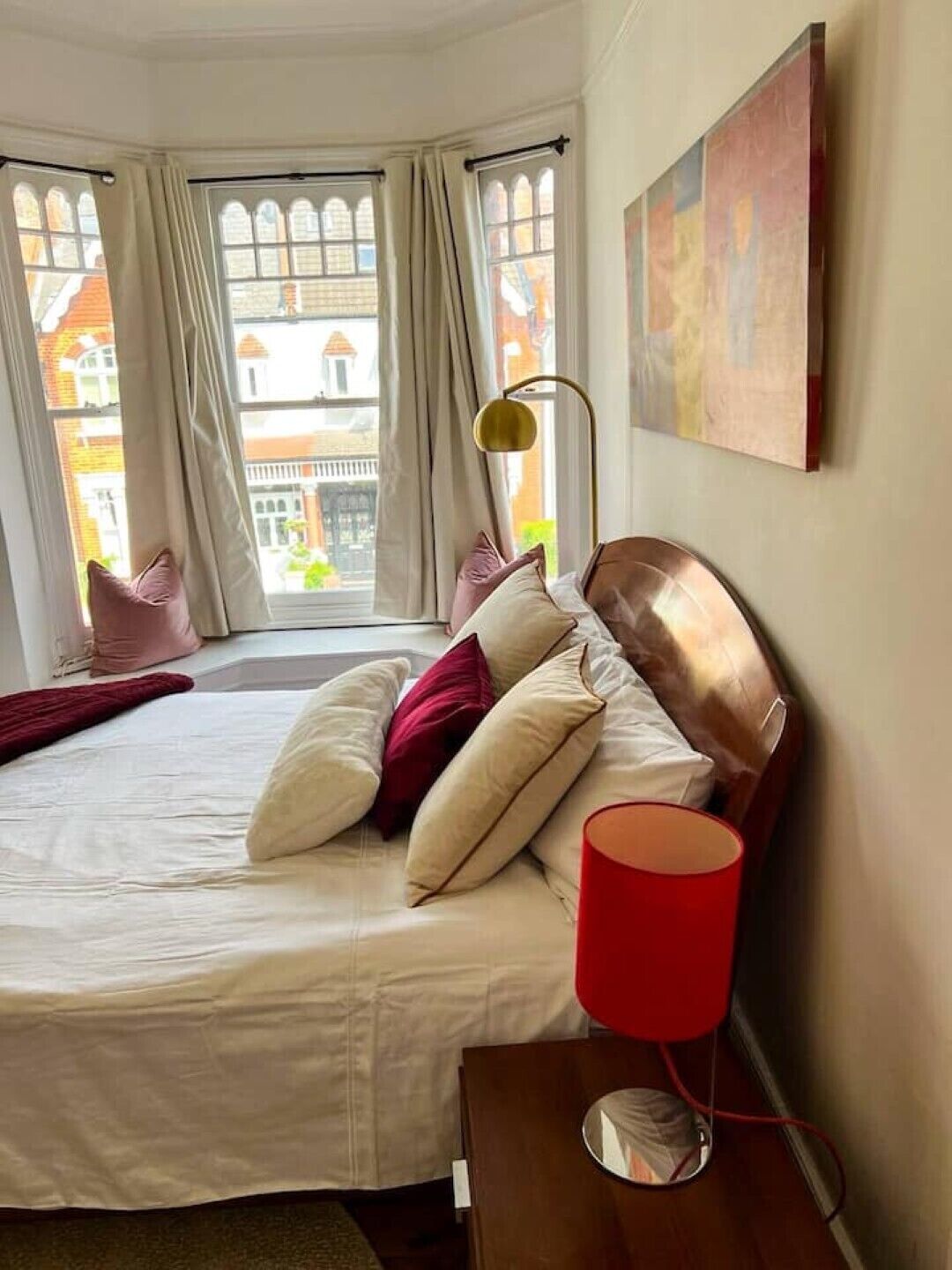 Habitación de hotel con cama, una lámpara roja y vistas de edificios a través de la ventana.